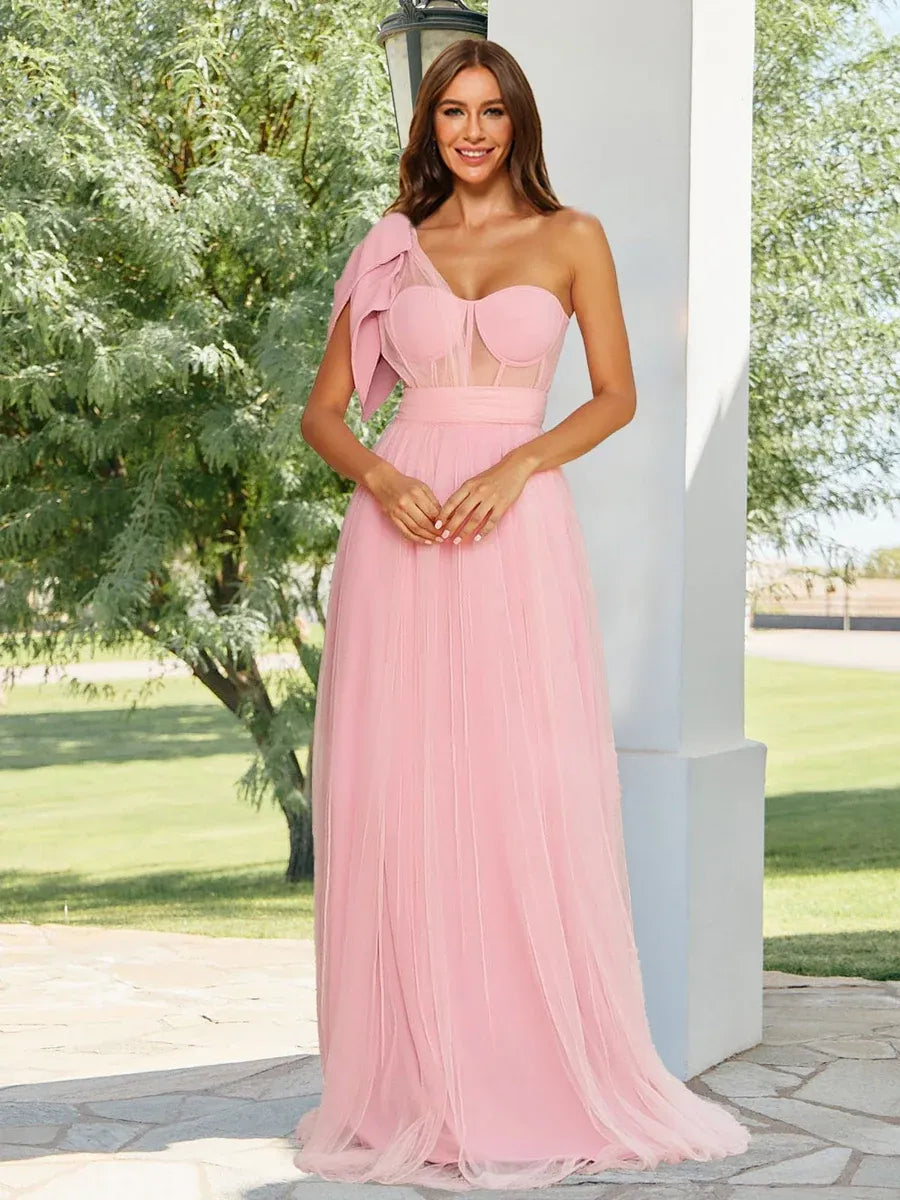 Front view of Loverlm blush pink one-shoulder bridesmaid dress with sweetheart neckline, oversized bow and floor-length tulle skirt